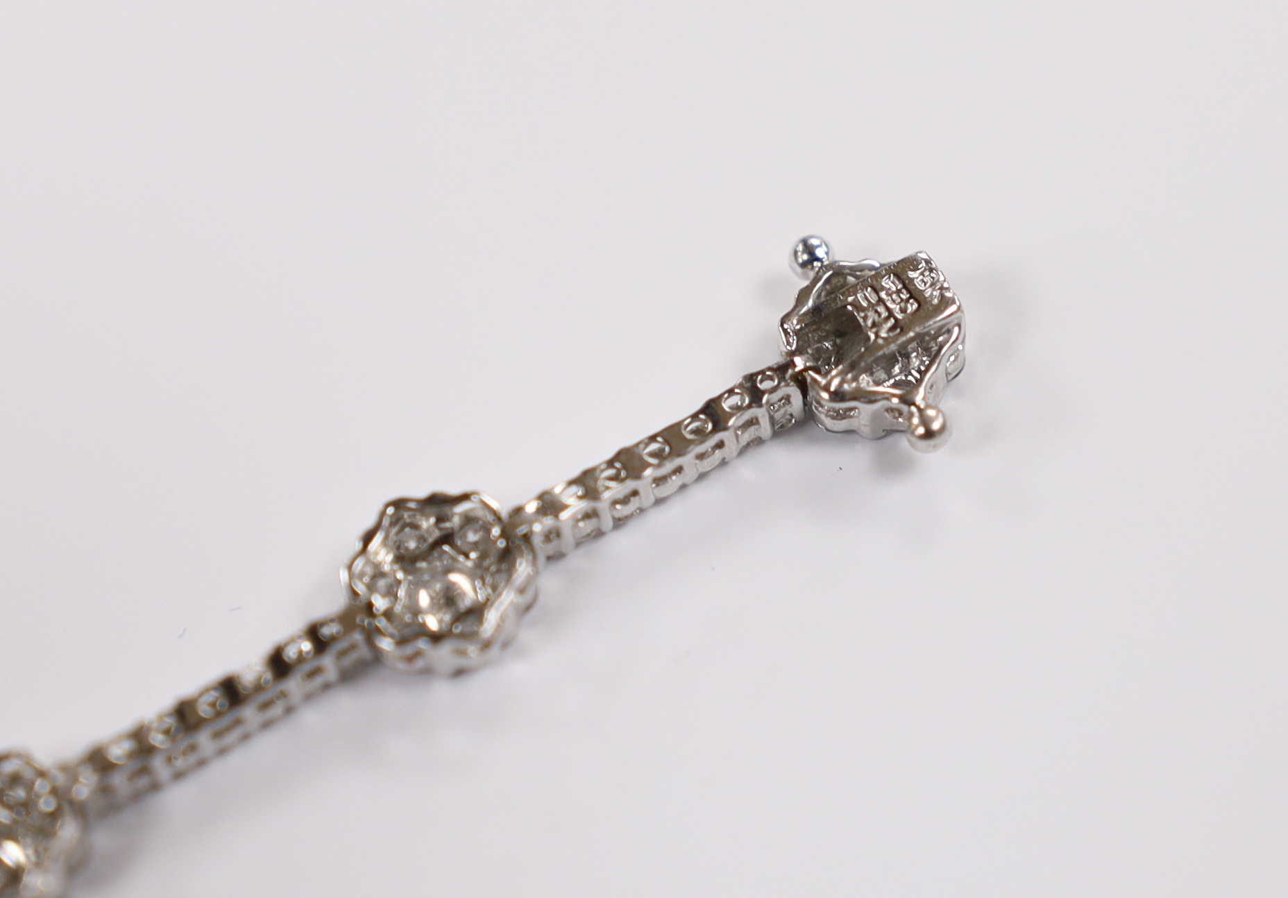 A modern 18k white metal and diamond cluster set flower head line bracelet, 17.5cm, gross weight 8.4 grams.